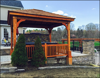 10 x 12 Cedar Ramada shown with custom 2x2 Straight Spindle Gazebo Railings with Newel Posts, Cedar Shake Shingles, and Cedar Stain Sealer.In the background: 16 x 16 Treated Pine Deluxe 4-Beam Pergola with Cedar Stain/Sealer and 12" Top Runner Spacing12" Top Runner Spacing
