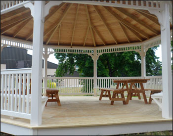 20 Vinyl Octagon Gazebo shown with a treated pine deck, 1x1 standard railings, standard braces, cupola, top railing sections, old english pewter asphalt shingles 4 bench sections, and two 6 Red Cedar Picnic Tables w/ Benches