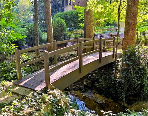 Heavy Duty 4 x 24 Double Rail Pedestrian Trail Bridge shown with Arched Glulam Beams, Woodland Brown Trex Decking, 36" tall Pine Double Railings, and customer-provided stain.